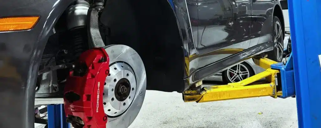 Expert brake repair and service in Gainsville, GA. Brakes and suspension repair with Atlanta Speedwerks. Car on a lift in a garage, tire removed, showing a red brake caliper and rotor.