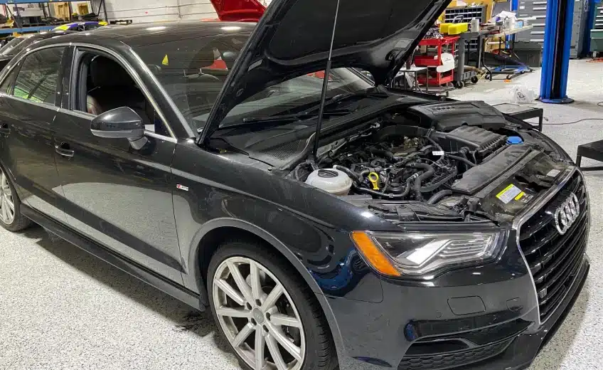 A black Audi car with its hood open inside a garage service area.