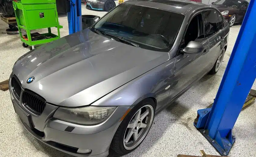 Silver BMW sedan in a garage on a car lift, with a green tool chest nearby.