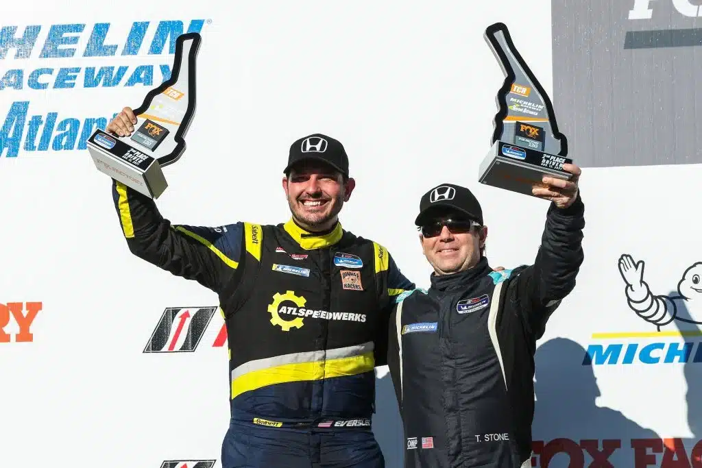 two men in racing suits holding trophies