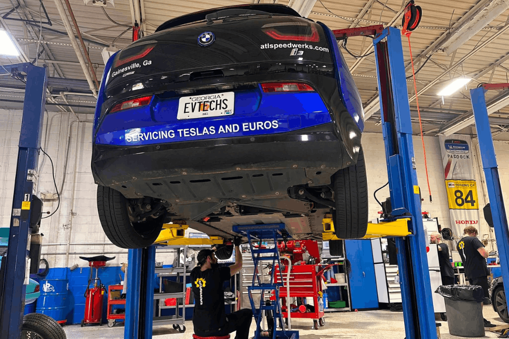 EV battery upgrade, European auto repair in Gainesville, GA, at Atlanta Speedwerks. Image shows a BMW i3 on a lift while a technician performs professional electric vehicle service and inspection.
