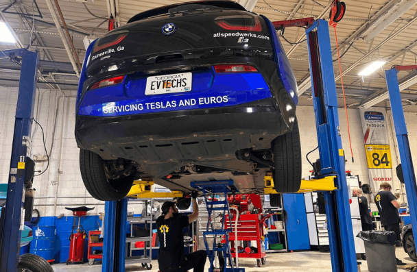 EV battery upgrade, European auto repair in Gainesville, GA, at Atlanta Speedwerks. Image shows a BMW i3 on a lift while a technician performs professional electric vehicle service and inspection.
