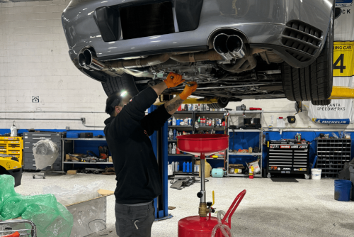 Oil change services in Gainesville, GA by Atlanta Speedwerks. Image of a technician working under a lifted sports car with an oil drain pan, highlighting the shop’s commitment to performance, precision, and engine longevity.