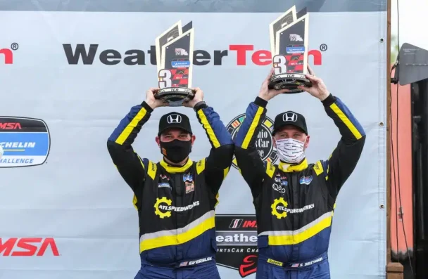 two men in race suits holding trophies